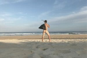 Un homme pose nu de dos sur la plage avec un sac poubelle