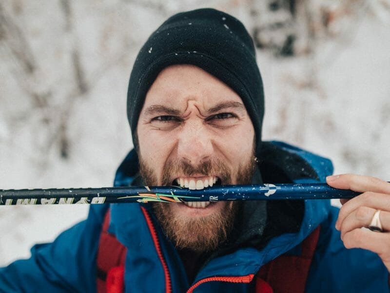 un homme sur un chemin enneigée tient dans sa bouche son bâton de ski