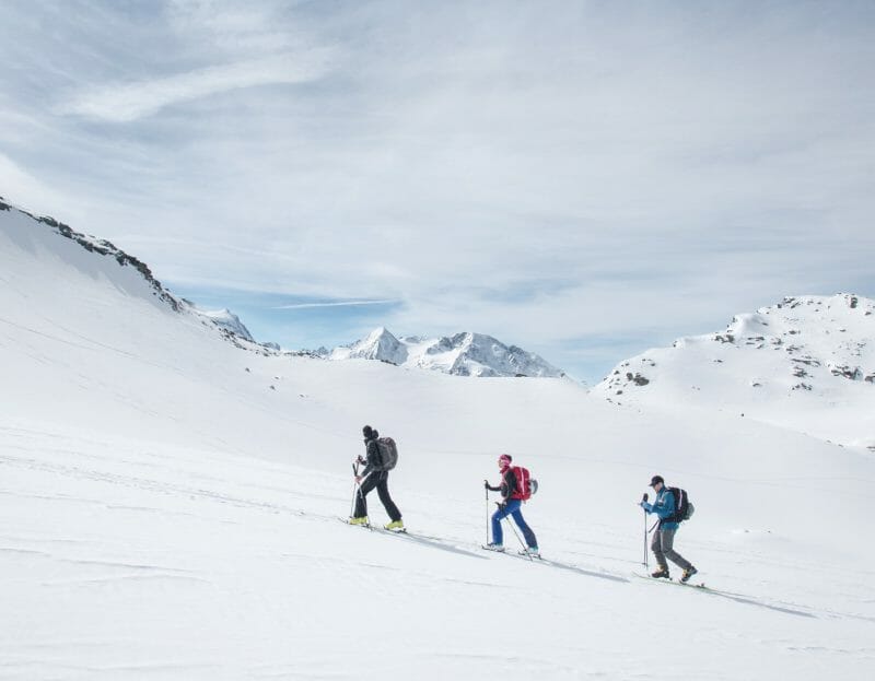 3 skieurs randonnent dans la neige sous le soleil