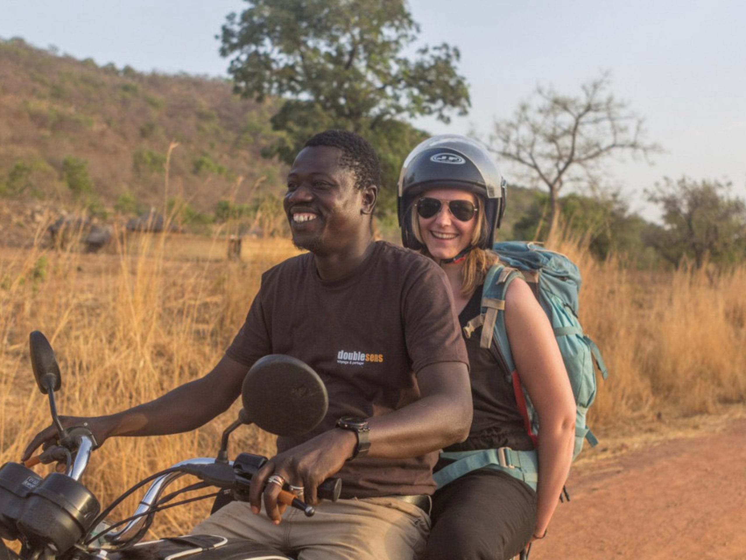 Un béninois et une voyageuse sur un scooter dans la savane