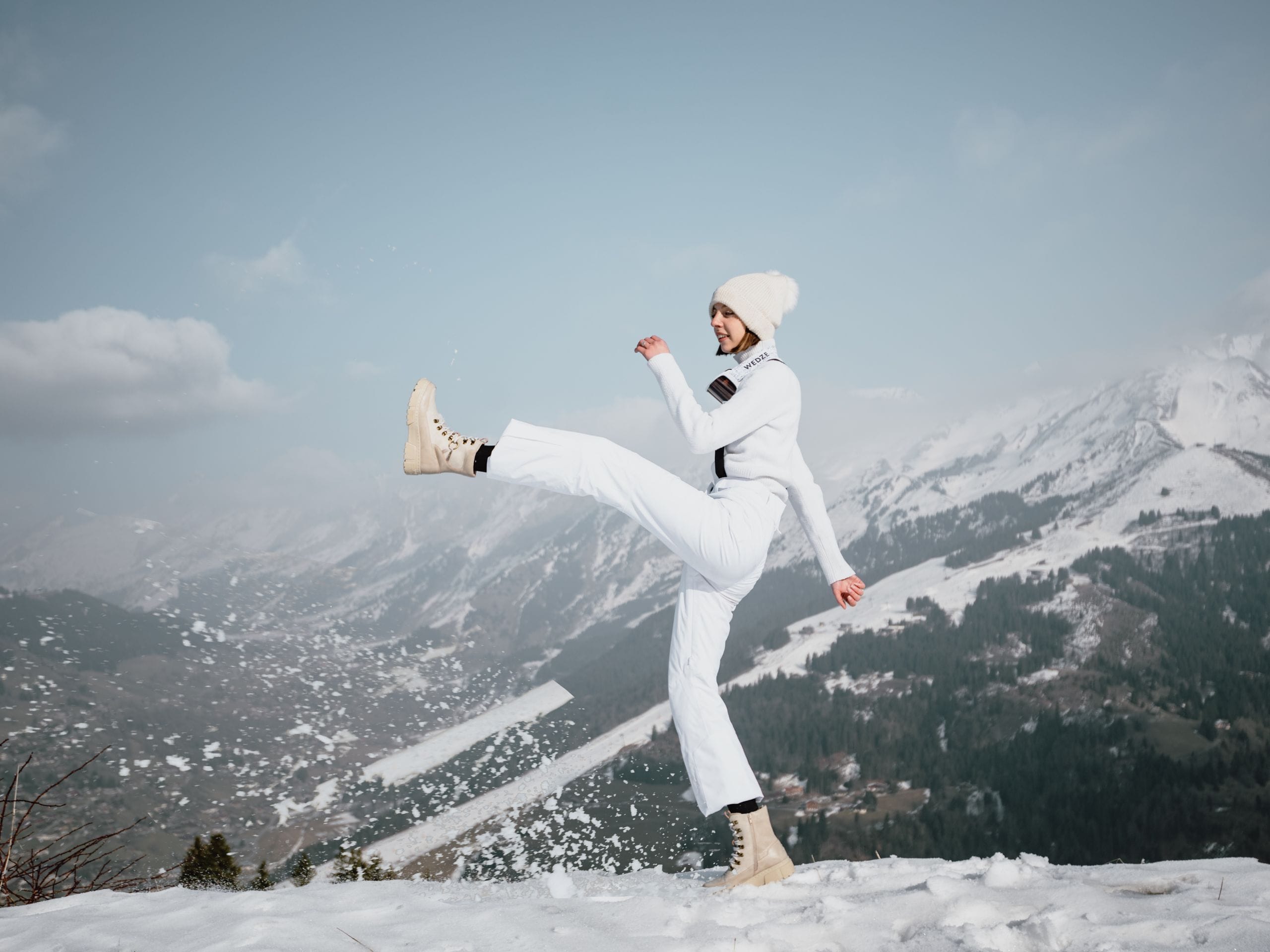 Une femme avec sa jambe droite levée en l'air, dans la neige.