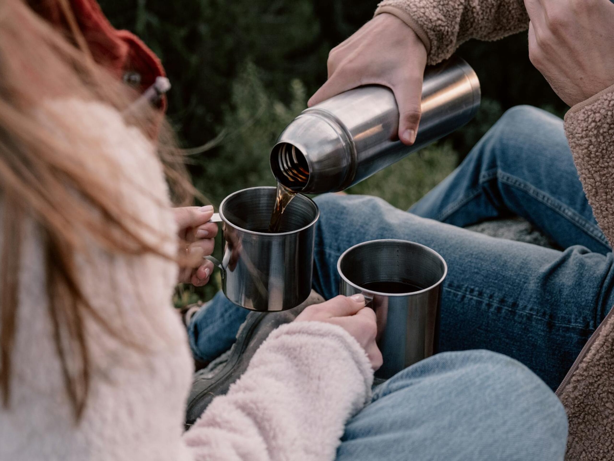 Deux personnes qui partage un thermos de café en pleine nature. 