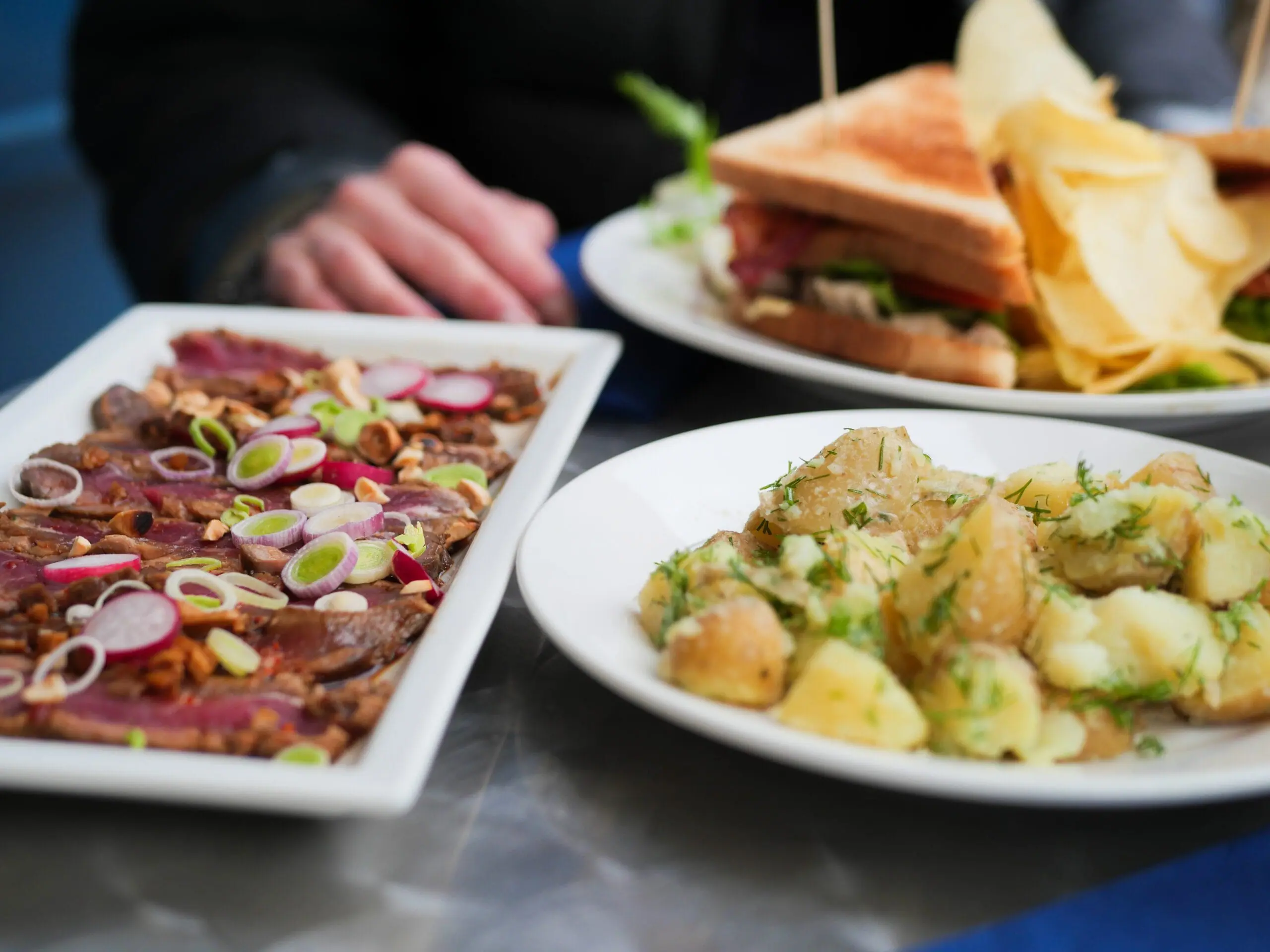 Assiette de tataki de boeuf avec salade de pommes de terre, et club sandwich en fond