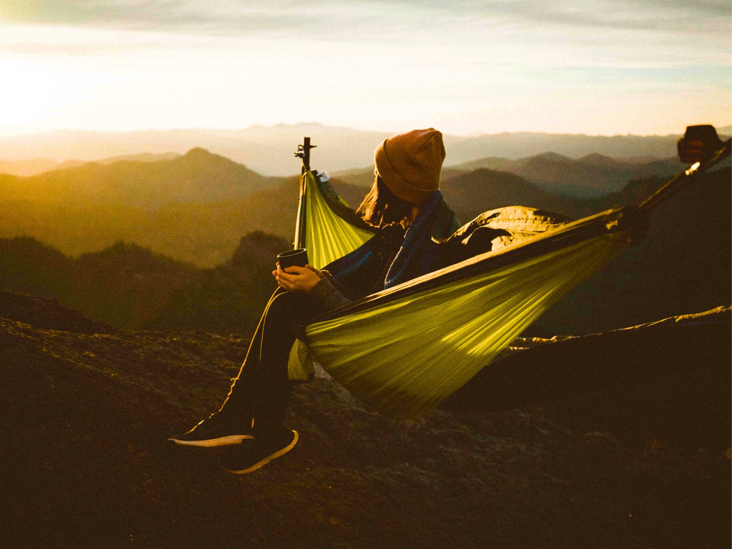 Une jeune femme quin contemple le paysage montagneux assise dans un hamac